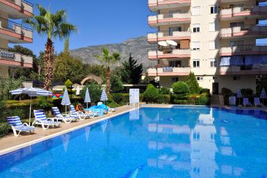 Χαλάρωση δίπλα στην πισίνα σε ένα ηλιόλουστο συγκρότημα διαμερισμάτων στην Αλάνια με θέα στο βουνό.